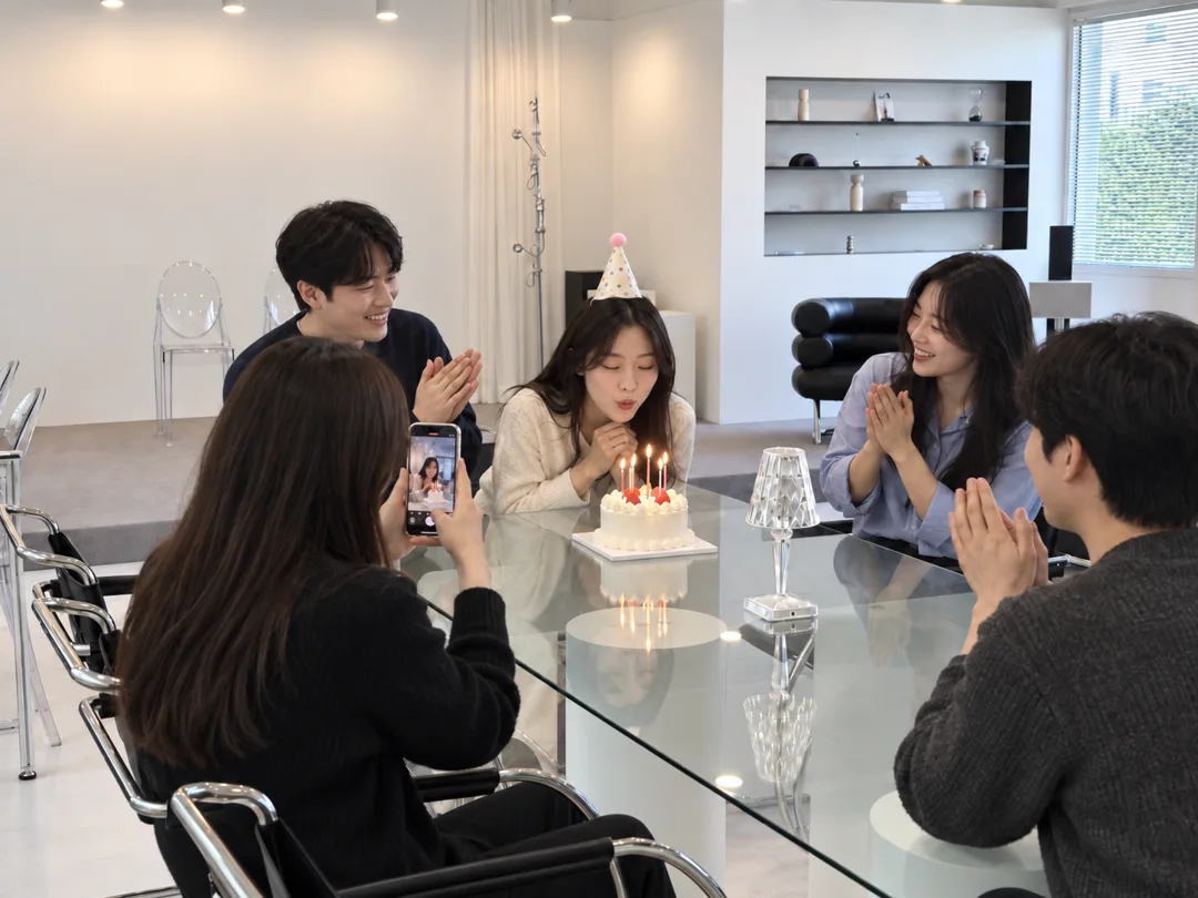 다이닝 테이블에서 생일 케이크 촛불을 부는 친구들